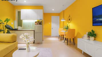 A modern living room with a yellow sofa, a white coffee table with flowers, and a dining area with yellow chairs.
