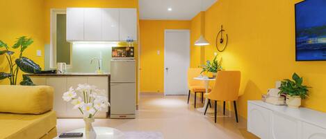 A modern living room with a yellow sofa, a white coffee table with flowers, and a dining area with yellow chairs.