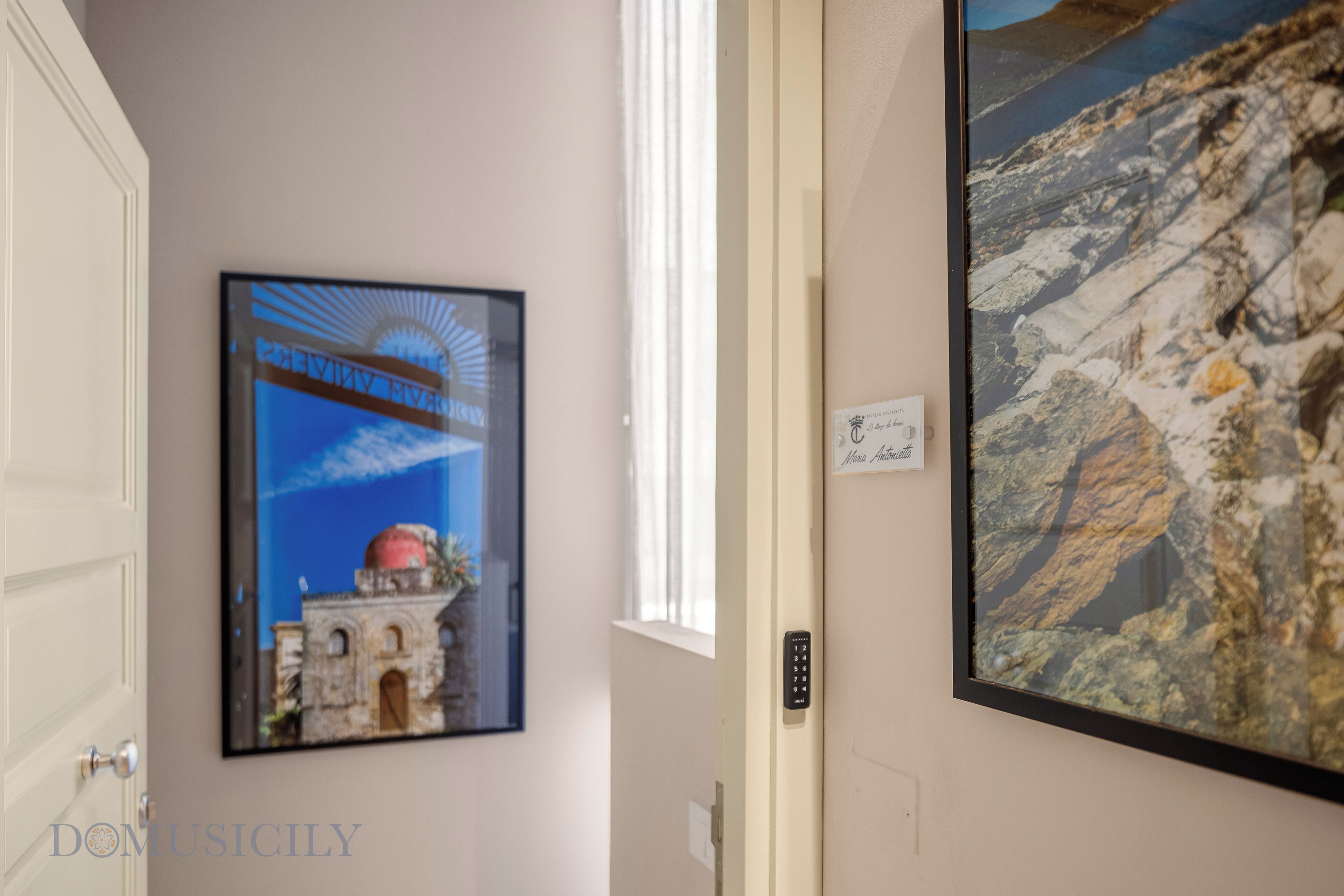 A hallway with a framed picture of a historical building, a large framed geological map, and a door with a keypad lock.