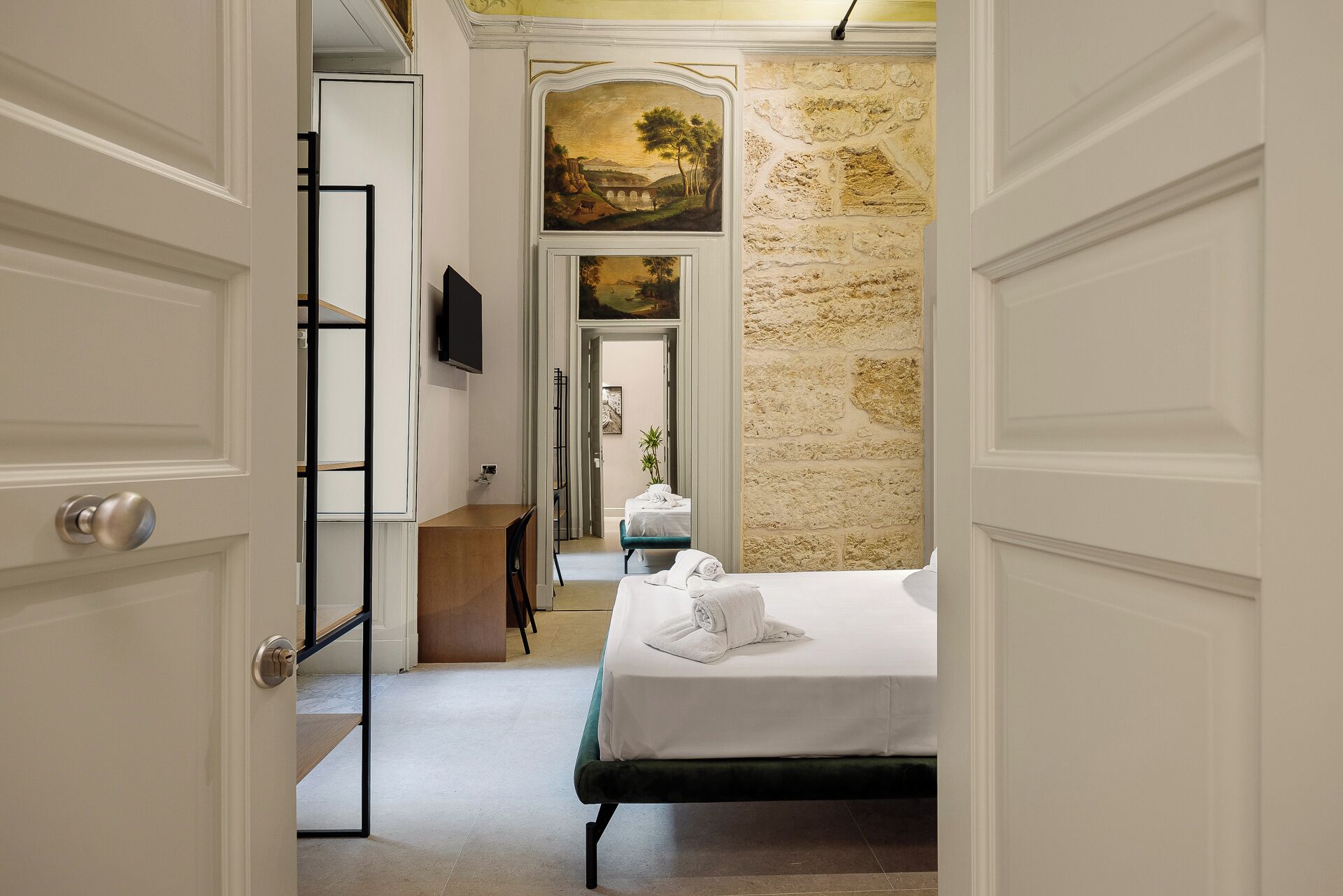 Une chambre d’hôtel avec un lit, un bureau, une télévision et un mur en pierre.