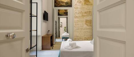 A hotel room with a bed, a desk, a TV, and a stone wall.