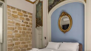 Een slaapkamer met een stenen muur, een bed met witte lakens, een grote spiegel en een deur.