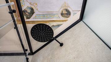 A corner of a room with a glass partition, a black circular object with holes, and a tiled floor.