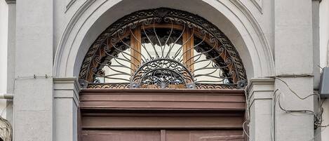 Una puerta doble marrón con ornamentación metálica detallada y un arco decorativo encima.