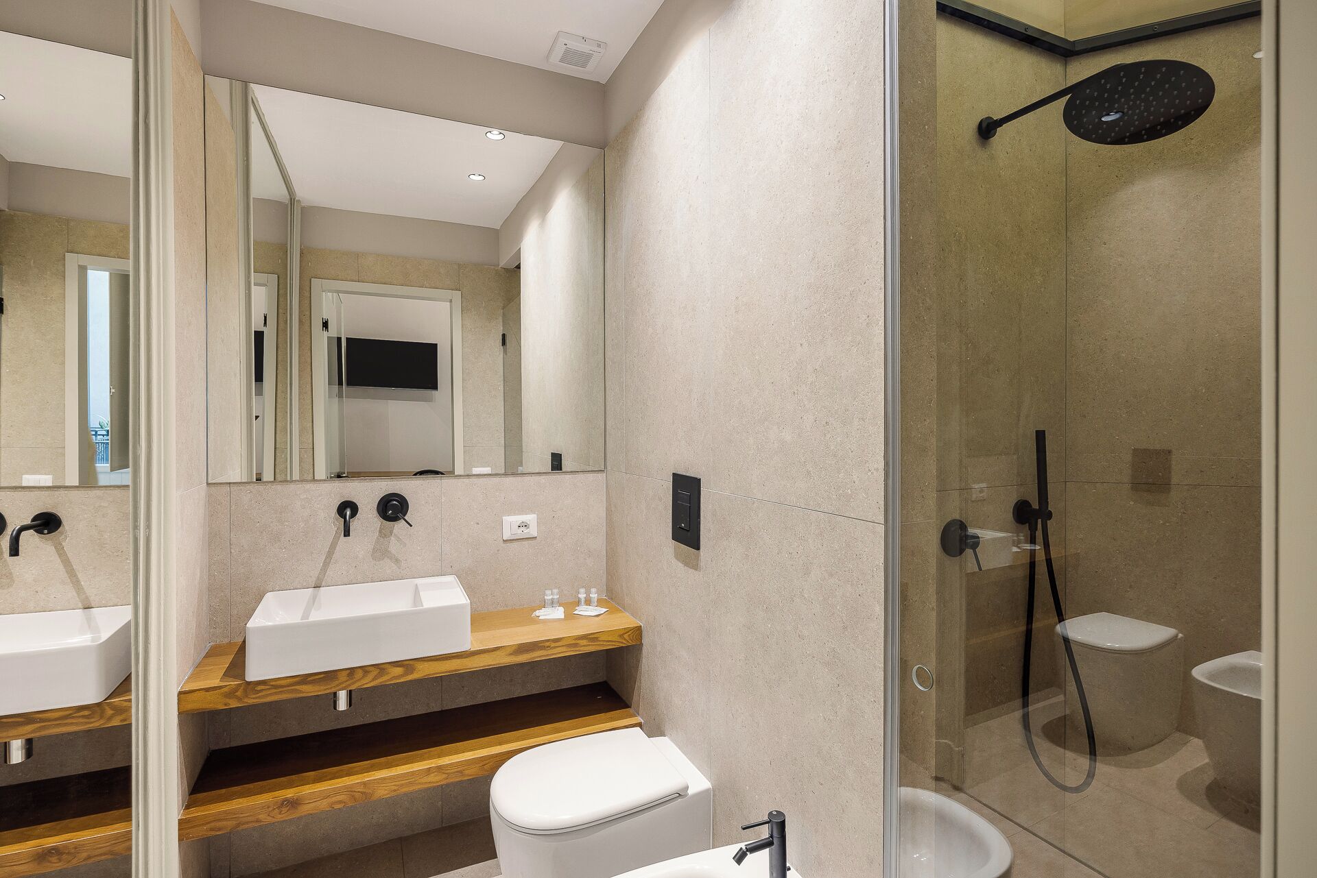 Un baño moderno con ducha envuelta en vidrio, tocador de madera y un inodoro blanco.