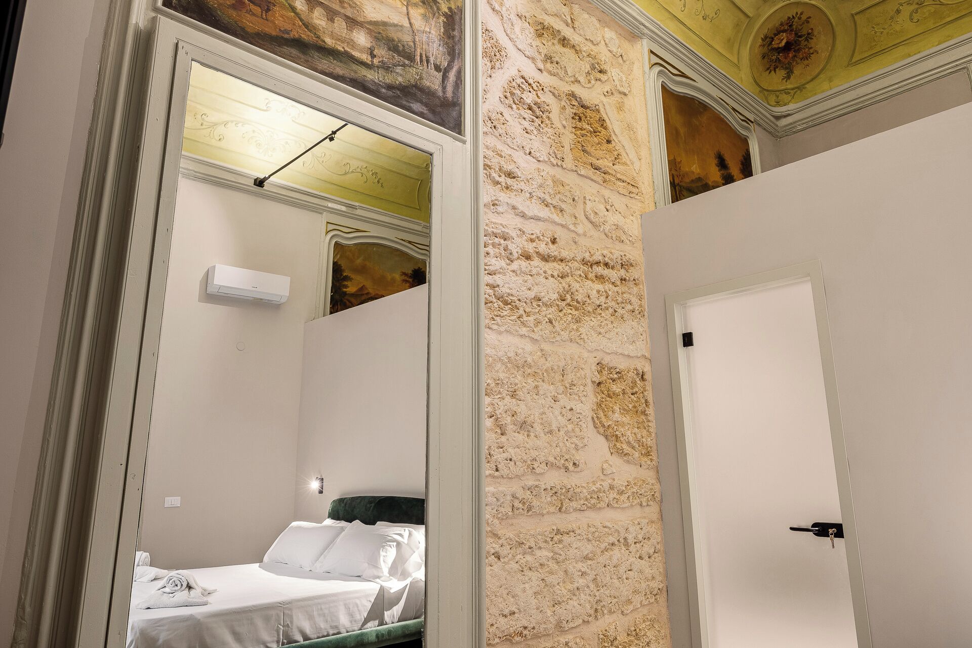 A room with a bed, a mirror, a door, and a textured wall.