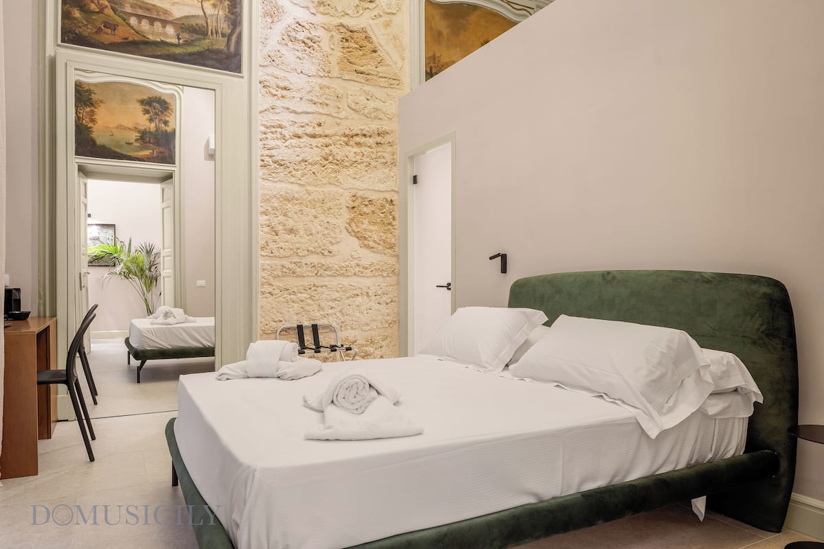 Un dormitorio con cabecera tapizada en verde, ropa de cama blanca y una toalla sobre la cama.