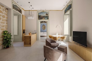 A modern living room with a TV, seating, a dining area, and a kitchen.