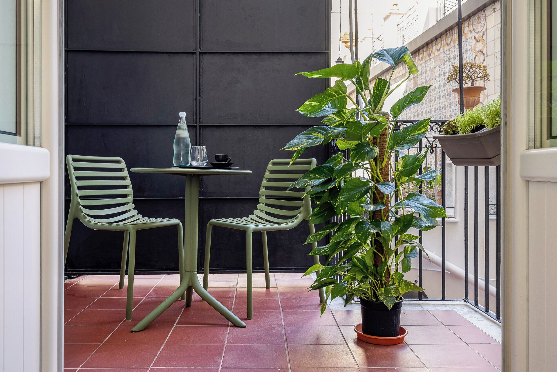 A small outdoor seating area with two chairs and a table, a potted plant, and a bottle and glass on the table.