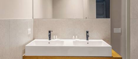 Un baño moderno con lavamanos doble, repisas de madera y luces empotradas en el techo.