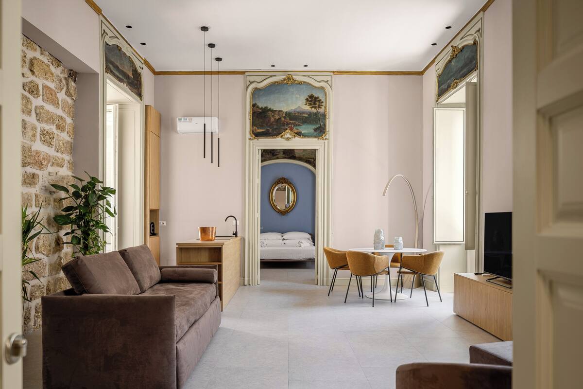 Una sala moderna con un sofá, una mesa de comedor con sillas, un televisor y un espejo grande.