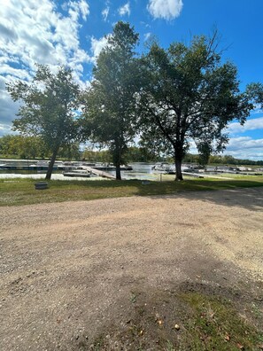A gravel area with trees and a body of water in the background.