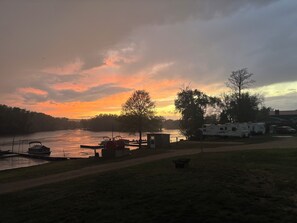 A riverside campsite with RVs, a dock with boats, and a small shed.