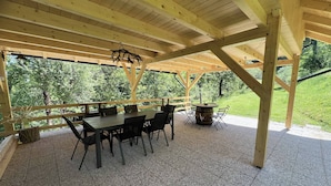 Une terrasse couverte avec une table et des chaises en bois, un tonneau et une vue sur un paysage verdoyant.