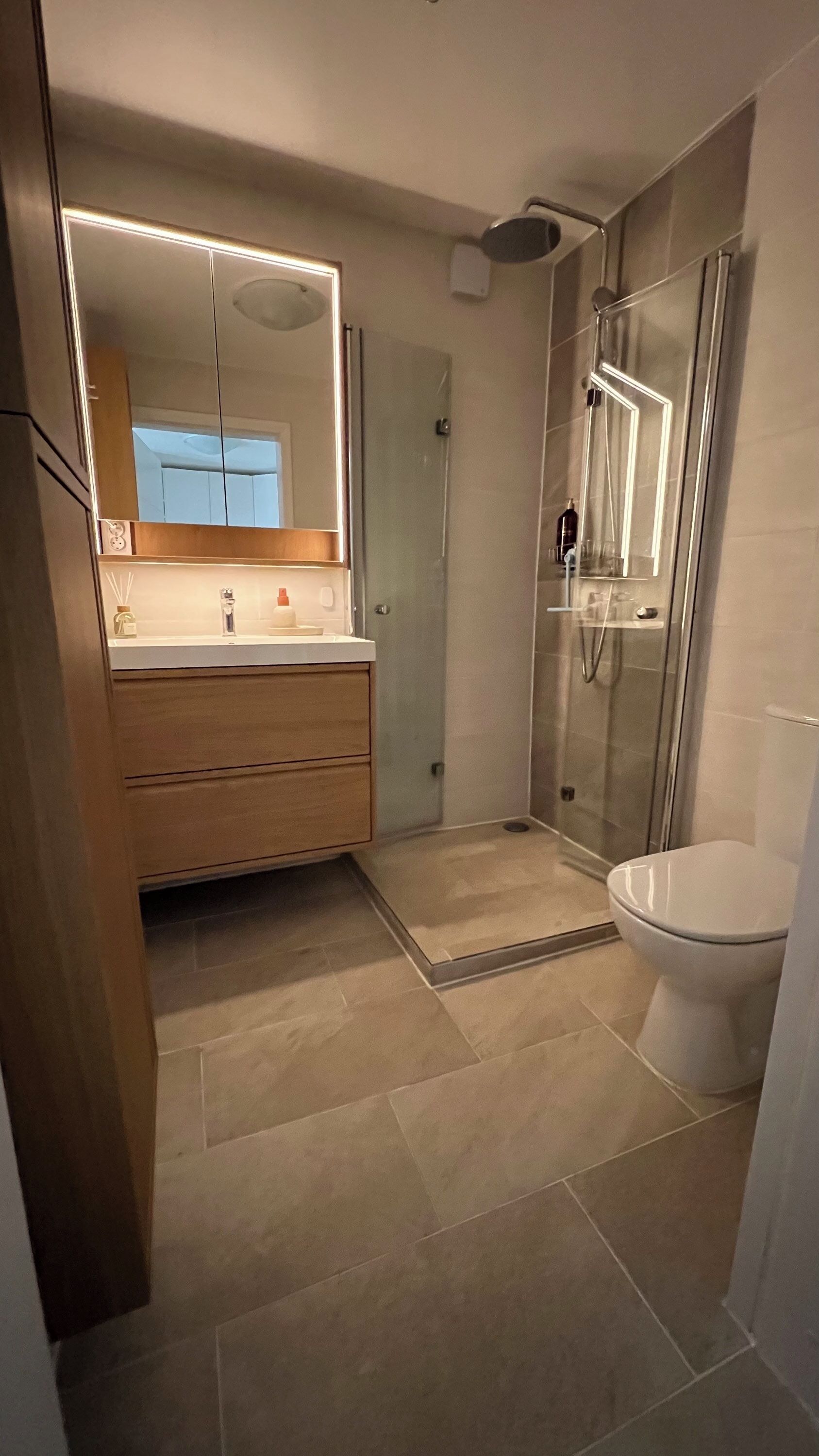 Un baño moderno con cabina de ducha de vidrio, inodoro y tocador con espejo.