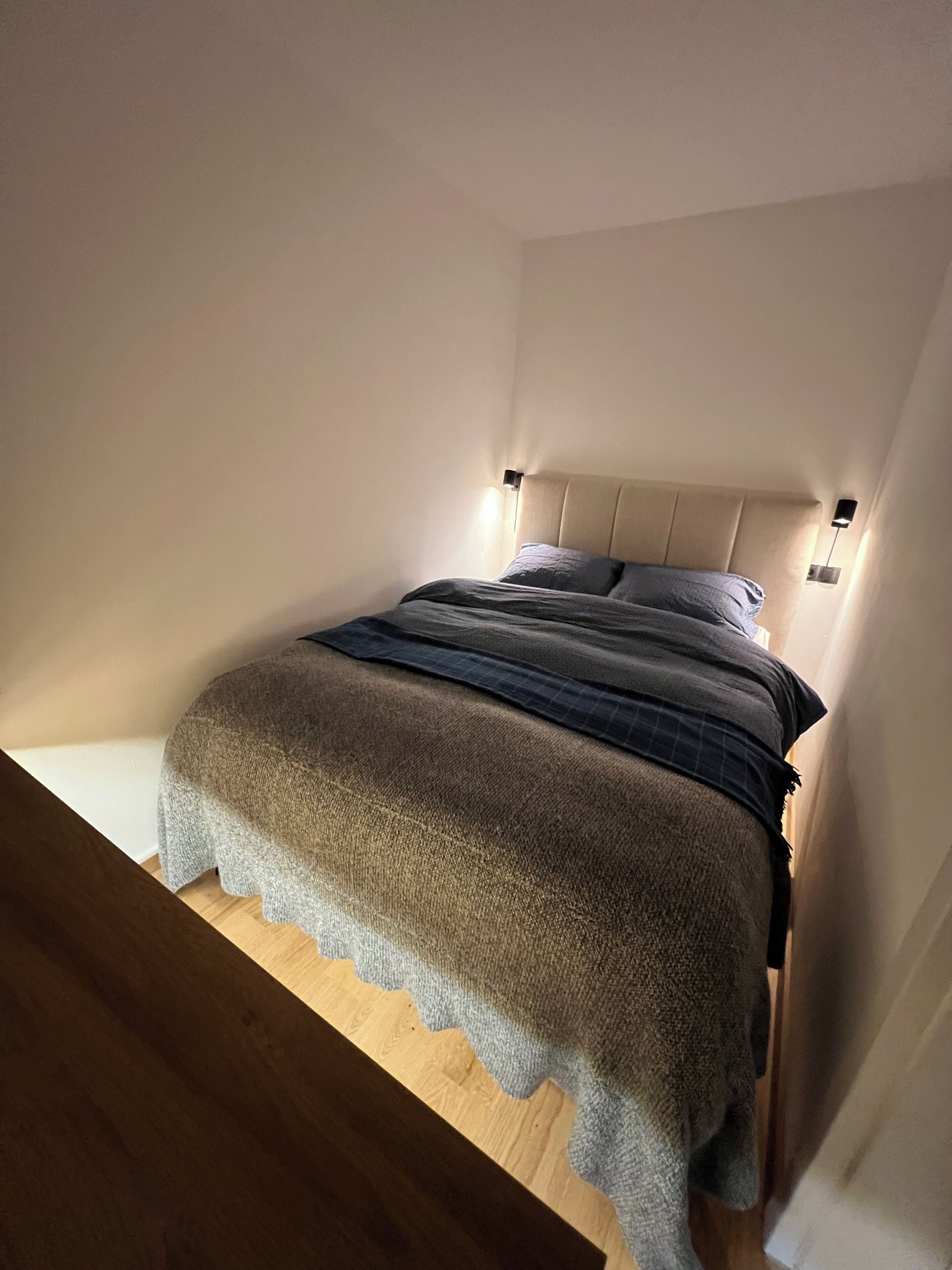 A single bed with a headboard, two bedside lamps, and a wooden floor.
