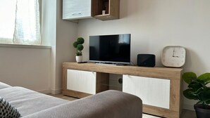 Una sala de estar moderna con una televisión de pantalla plana, un reloj y una planta en una consola de madera.