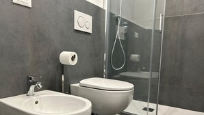 Un baño moderno con bidé, inodoro y cabina de ducha de vidrio.