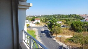 A balcony with a view of a road, greenery, and distant buildings.