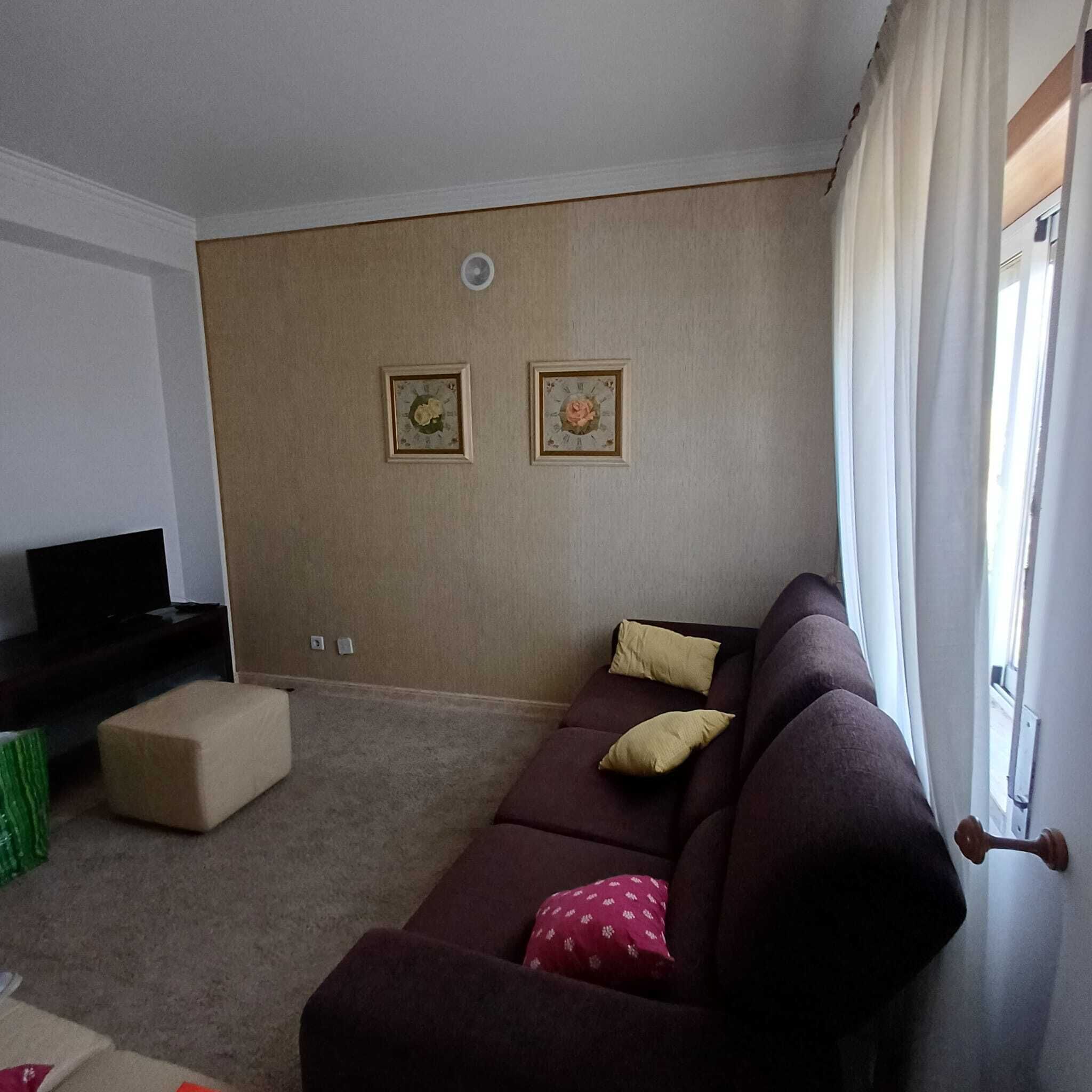 A living room with a dark brown sofa, beige ottoman, and two wall-mounted clocks with floral designs.