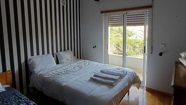 A bedroom with a bed, a ceiling fan, a window with blinds, and a view of greenery outside.