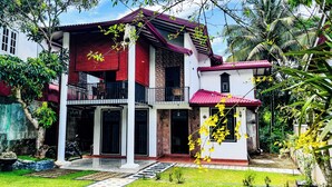 A two-story house with a balcony, a red roof, and a garden with yellow flowers. - Dadas Villa - A Private Villa in Kandy & Peaceful Escape for Families & Couples (Kundasale, Sri Lanka)
