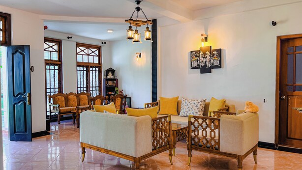 A spacious living area with a sofa set, wooden chairs, and a decorative wall piece. - Dadas Villa - A Private Villa in Kandy & Peaceful Escape for Families & Couples (Kundasale, Sri Lanka)