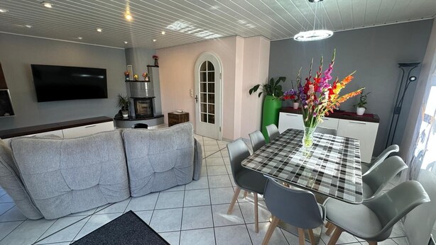 A modern living room with a sofa, a dining table with chairs, a fireplace, and a TV mounted on the wall. - Modern and comfortable house in Nidderau - ideal for families and couples (Nidderau)