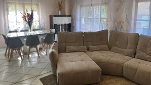 A modern living room with a sectional sofa, a dining table with chairs, and a kitchen area with a refrigerator. - Modern and comfortable house in Nidderau - ideal for families and couples (Nidderau)
