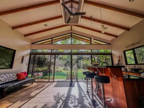 A modern kitchen with a bar area, large sliding glass doors leading to a garden, and a ceiling fan. - Private Riverfront with 2-Acre Organic Food Forest (San Isidro de El General)