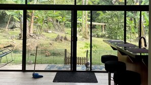 Une pièce spacieuse dotée de grandes fenêtres, d’un coin cuisine et offrant une vue sur un jardin luxuriant.
