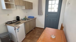 A compact kitchen with a small refrigerator, a coffee maker, and a sink. There's a blue door with a window, a wooden table, and a chair. - Leon Lux Apartment, double room. (Emporio)