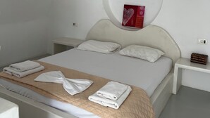 A bedroom with a bed, white bedding, a towel on the bed, a bedside table with a lamp, and a wall-mounted light fixture. - Leon Lux Apartment, double room. (Emporio)