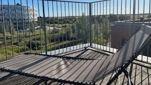 Un balcone con ringhiera in metallo, una sedia imbottita e vista su un edificio e vegetazione.