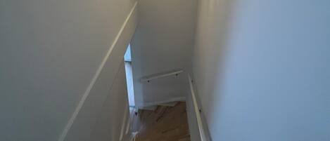 A narrow staircase with wooden steps and white walls.