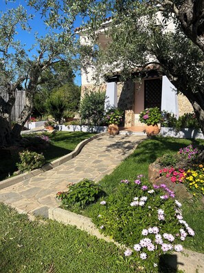 Un sentier de jardin qui mène à un bâtiment aux murs en pierre et au toit recouvert de tuiles.