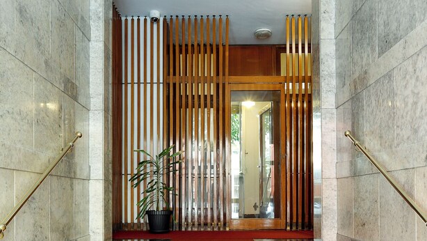 A marble staircase with a red carpet leading to a door with vertical blinds.