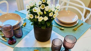 A dining table set with plates, cutlery, and glasses, with a potted plant in the center.