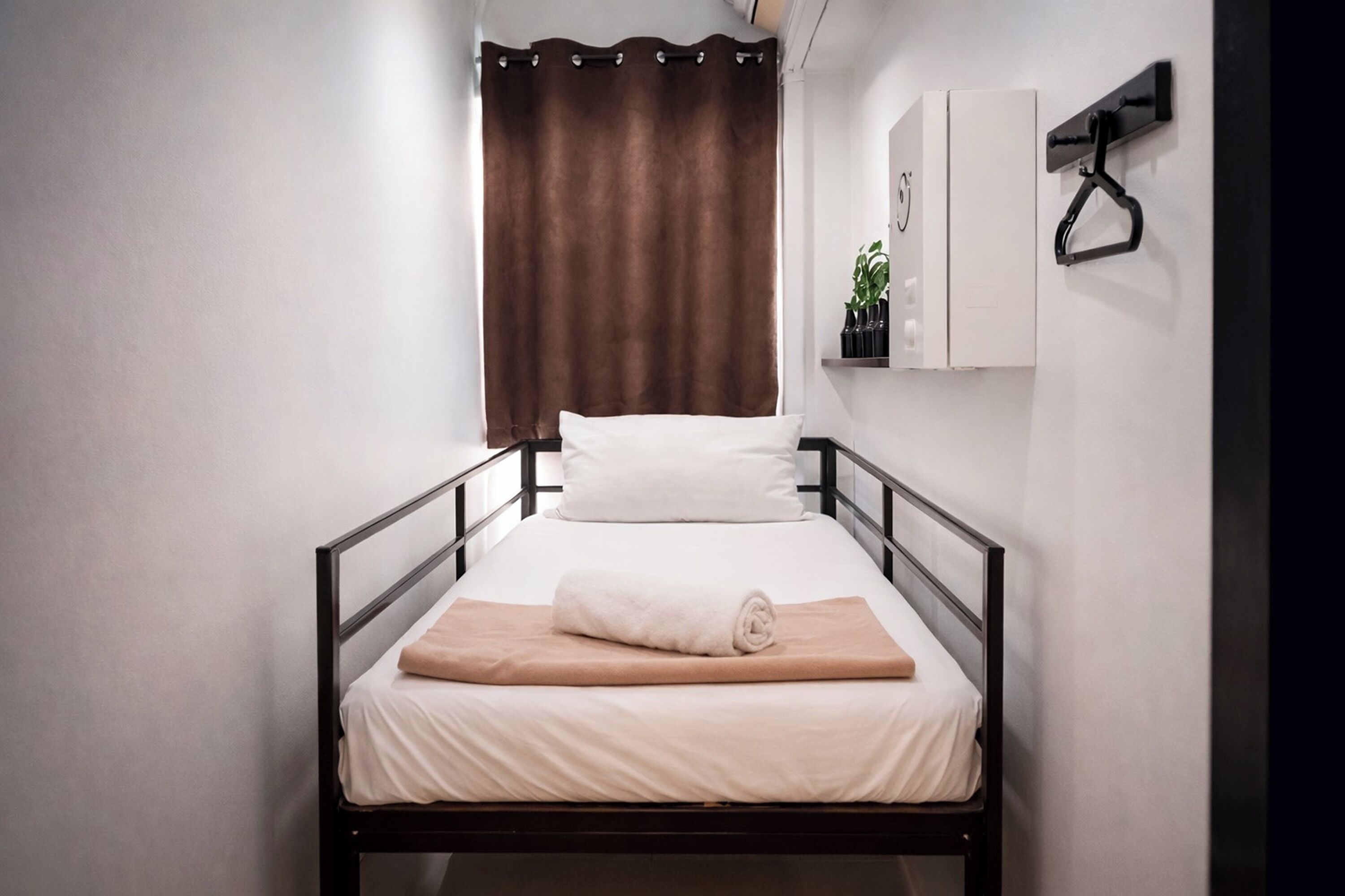 A single bed with a white mattress, a beige blanket, and a brown curtain.