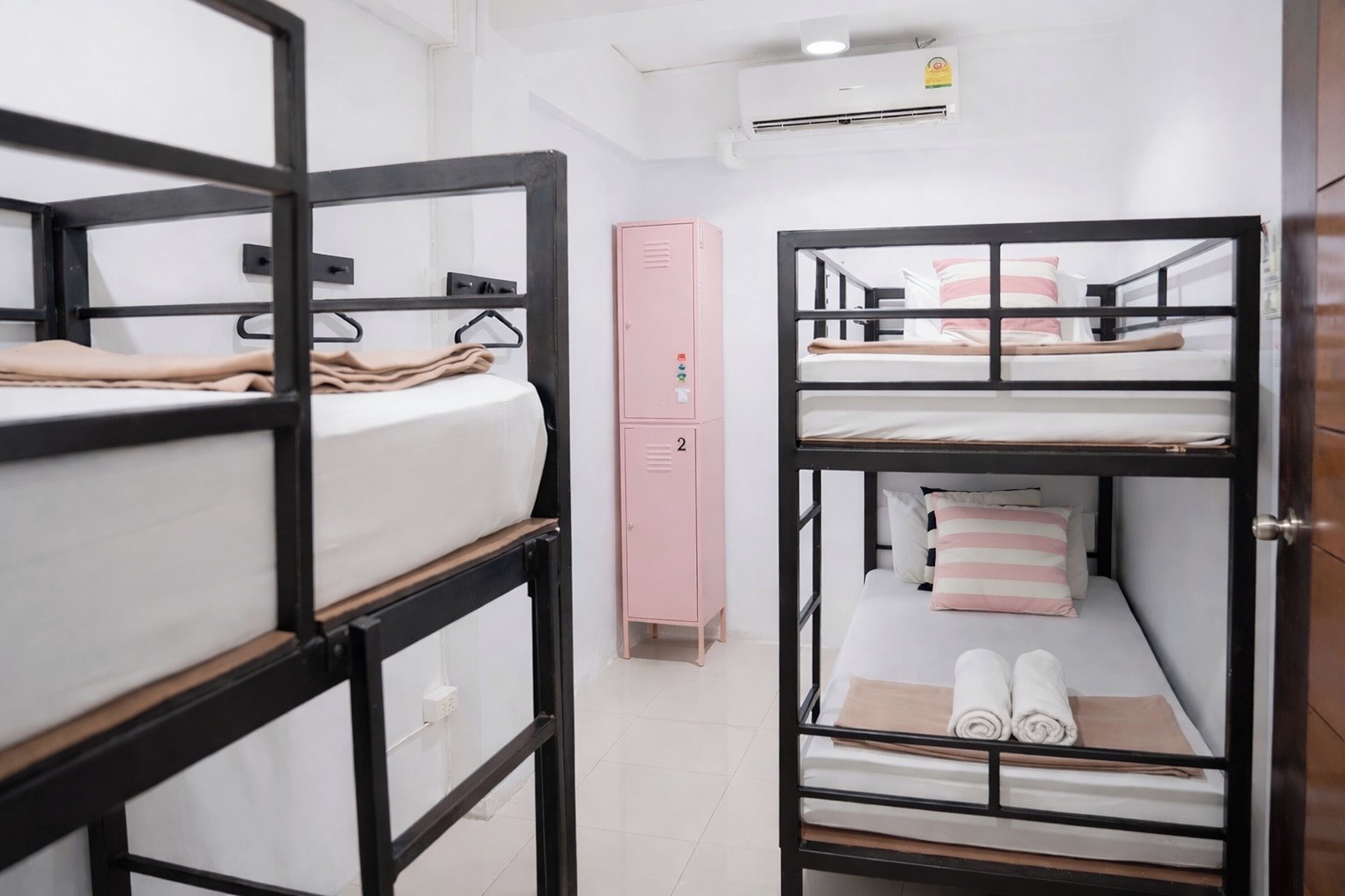 A dormitory room with bunk beds, a pink storage unit, and a white wall with an air conditioning unit.