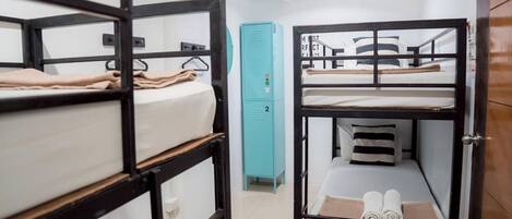 Ein Schlafsaalzimmer mit Etagenbetten, einem türkis-farbenen Stauraum und einer weißen Tür.