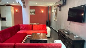 A living room with a red sofa, a white sofa, a coffee table, a TV, and a fireplace. - Riad 3 rooms 306m2 500 m from Place Jemaa el-Fna (Marrakech)