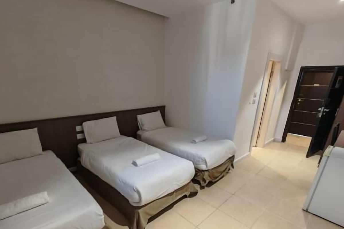 A hotel room with two single beds, a small kitchenette, and a door leading to a hallway.