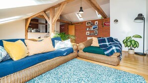 A cozy loft bedroom with a sloped ceiling, exposed wooden beams, a blue sofa, and a brick wall adorned with photos. - Bright and airy apartment in unique suburb (Praha 3)