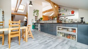 A modern kitchen with wooden beams, a dining area with a table and chairs, and a view of the living area. - Bright and airy apartment in unique suburb (Praha 3)