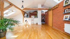 A spacious loft with high ceilings, exposed wooden beams, a kitchen area, and a brick wall with shelves. - Bright and airy apartment in unique suburb (Praha 3)