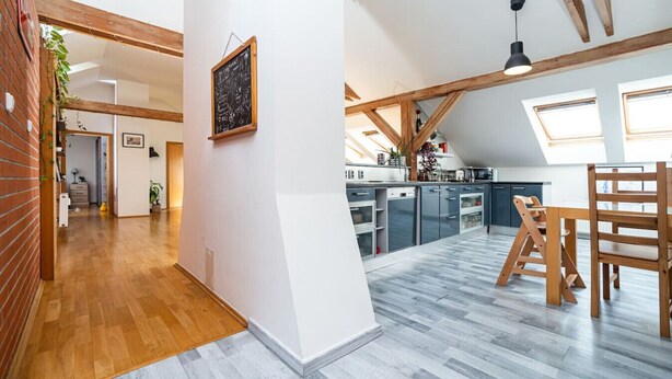 A spacious kitchen with high ceilings and skylights, a dining area with wooden furniture, and a hallway with a brick wall and wooden flooring. - Bright and airy apartment in unique suburb (Praha 3)