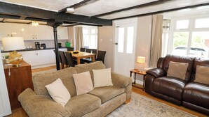 A living room with a sofa, a brown leather couch, a dining table with chairs, a kitchen area, and a window with curtains.