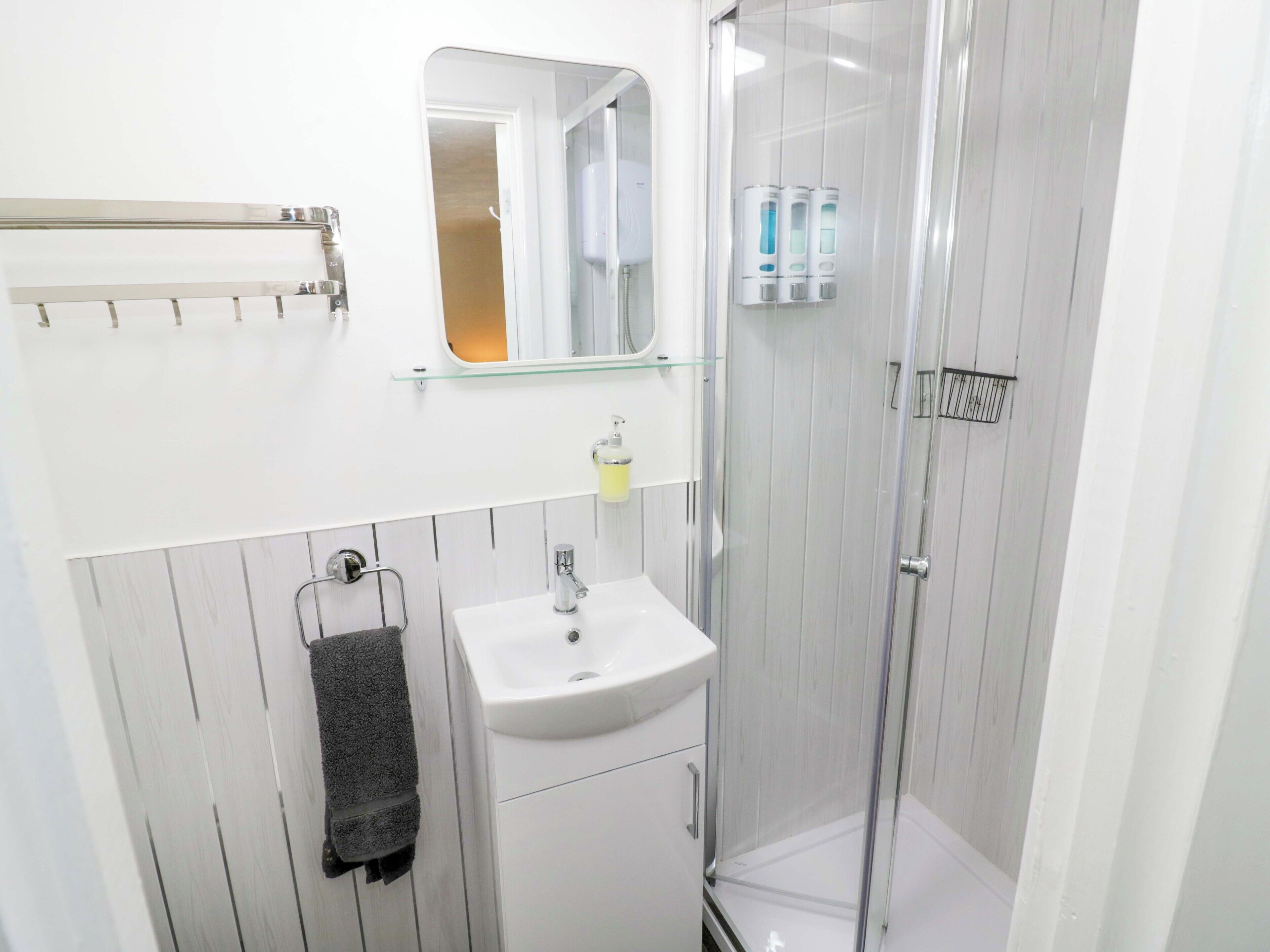 A modern bathroom with a glass shower enclosure, a white sink, and a towel rack.