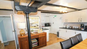 A compact kitchen with white cabinets, a microwave, and a coffee maker. There is a wooden dining table with chairs.